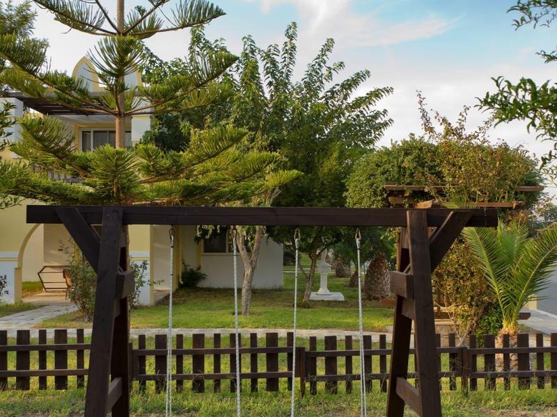 Houten schommel met twee zitplaatsen in tuin met bomen en hek op de achtergrond.