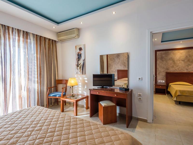 Moderne hotelkamer met tweepersoonsbed, tv, bureau en uitzicht op aangrenzende slaapkamer.