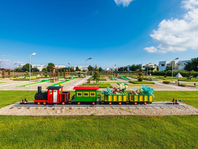 Kleurrijke miniatuurtrein op sporen voor grasveld en blauwe lucht.