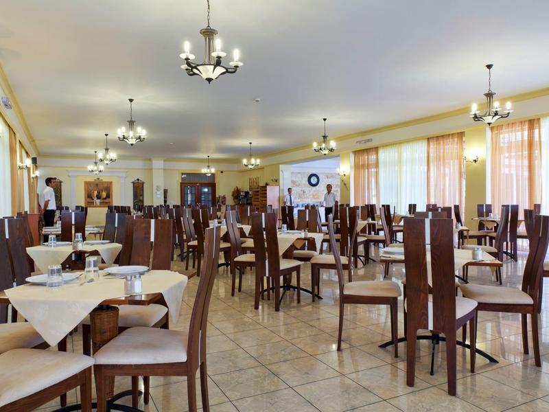 Grote, lichte eetzaal met veel houten stoelen en rechthoekige tafels.