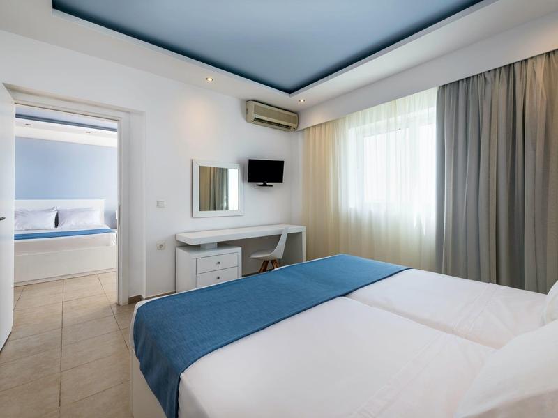 Moderne tweepersoonskamer met blauw bed, bureau, tv en toegang tot aangrenzende kamer.