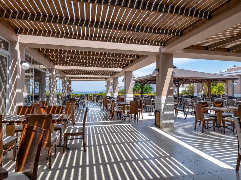 Ruim open eetgedeelte met houten meubels en schaduw van latten dak.