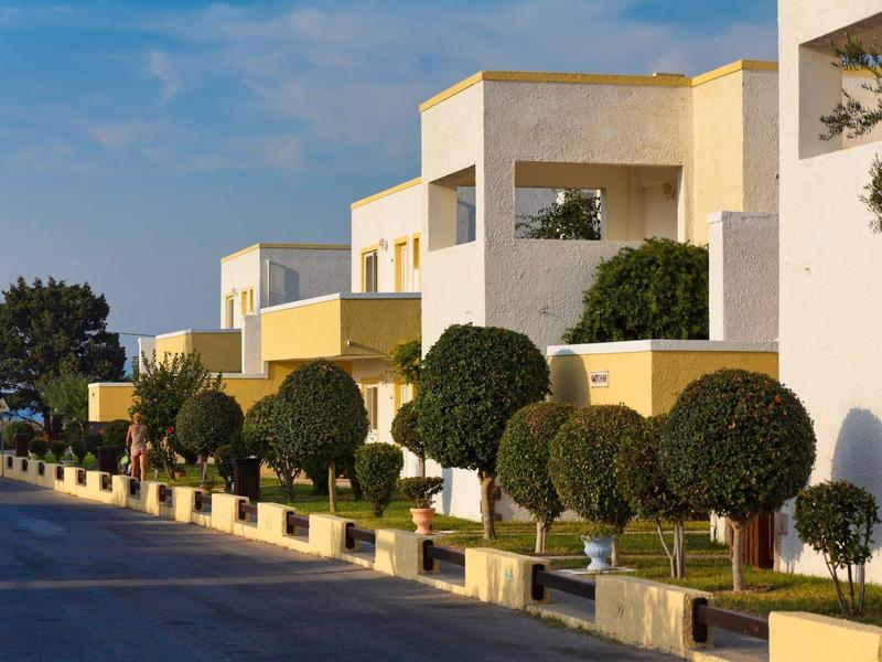 Moderne witte gebouwen met groene, ronde bomen langs een lege straat bij daglicht.