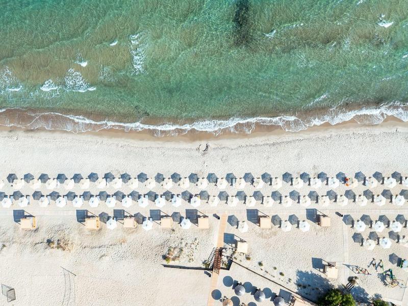 Luchtfoto van een strand met rijen parasols en turquoise water.