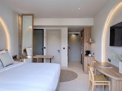 Licht ingericht hotelkamer met groot bed, bureau en aan de muur gemonteerde tv.