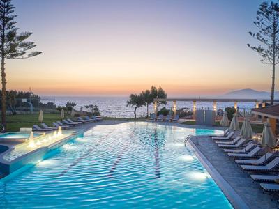 Ein beleuchteter Hotelpool mit Liegestühlen bei Sonnenuntergang am Meer.