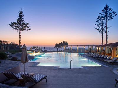 Een rustige zwembadomgeving bij zonsondergang met ligstoelen en uitzicht op zee.