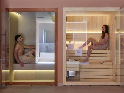 Zwei Frauen entspannen in modernen Saunen mit Glaswänden und Holzbänken.