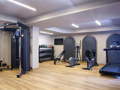 Moderner Fitnessraum mit Geräten wie Laufband und Ellipsentrainer, Holzboden und hellen Wänden.