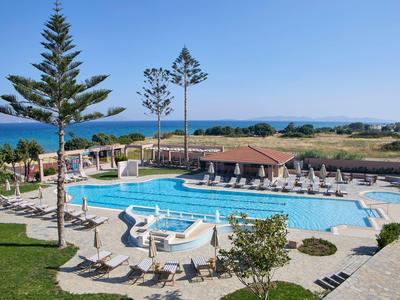 Groot buitenzwembad met ligstoelen, parasols en uitzicht op zee bij heldere lucht.