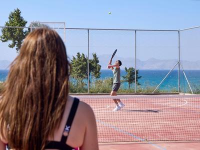 Eine Frau beobachtet einen Mann, der auf einem Tennisplatz am Meer Tennis spielt.