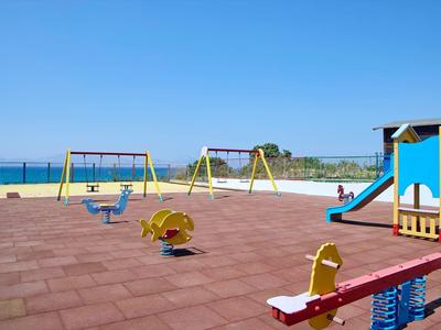 Speeltuin aan zee met kleurrijke schommels, glijbaan en wip onder een heldere hemel.