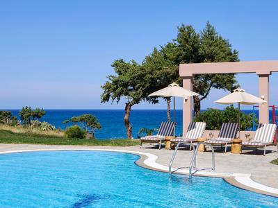 Runder Pool mit Liegestühlen und Sonnenschirmen vor Meer und blauem Himmel.