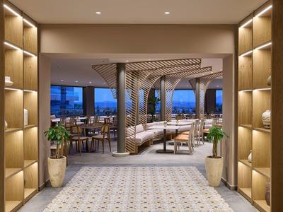 Moderne hotelgang met planken, planten en zithoek met gestoffeerd meubilair in neutrale tinten.