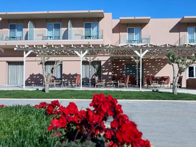 Hotelgebäude mit Balkonzimmern, Gartenbereich und roten Blumen im Vordergrund bei strahlendem Himmel.