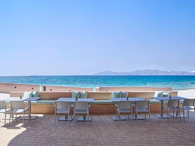 Tafels en stoelen op een terras met uitzicht op de zee en heldere lucht.
