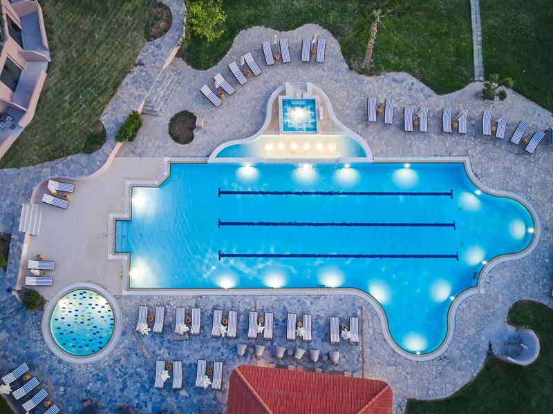 Verlicht hotelzwembad met ligstoelen en tuin vanuit vogelperspectief 's nachts.