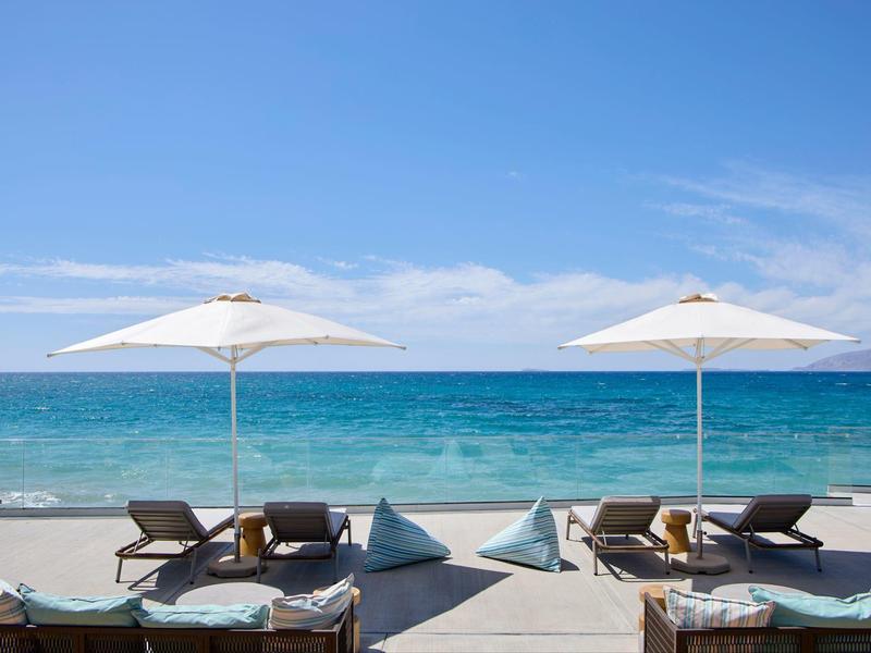 Uitzicht op twee parasols en ligstoelen aan zee met blauwe lucht.