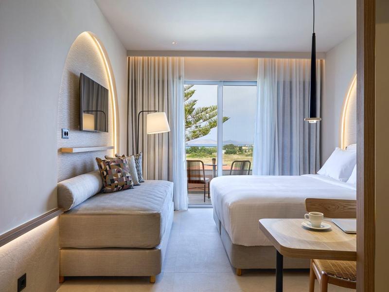 Modern hotelkamer met tweepersoonsbed, bank, zeezicht en balkon.