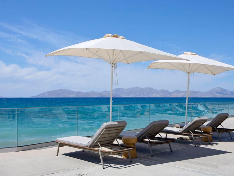 Drie ligstoelen met parasols op een terras met uitzicht op zee en bergen op de achtergrond.