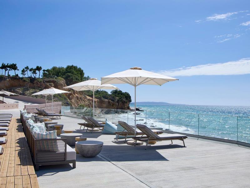 Moderne ligstoelen en parasols op een terras met uitzicht op zee bij heldere lucht.