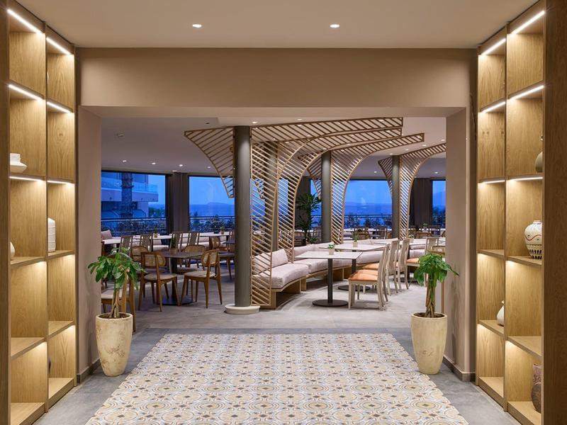 Moderne hotelgang met planken, planten en zithoek met gestoffeerd meubilair in neutrale tinten.