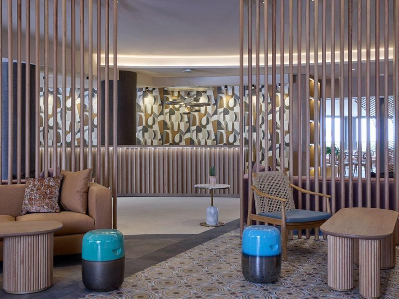 Moderne hotel-lounge met houten accenten en kleurrijke krukken in een lichte omgeving.