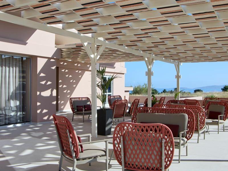 Overdekt terras met rode stoelen en tafels met uitzicht op de zee.