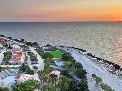 Küste bei Sonnenuntergang mit Strand, Wellen, Gebäuden und grün bewachsenen Bereichen.