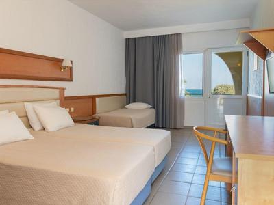 Helles Hotelzimmer mit Doppelbett, Einzelbett, Schreibtisch, Stuhl und Balkon mit Meerblick.