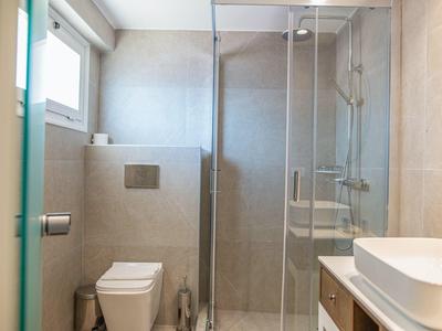 Kleines modernes Badezimmer mit Glasdusche, Toilette, Waschbecken und grauen Fliesen.