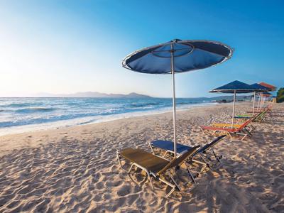 Leerer Strand mit blauen Sonnenschirmen und Liegestühlen bei klarem Himmel.