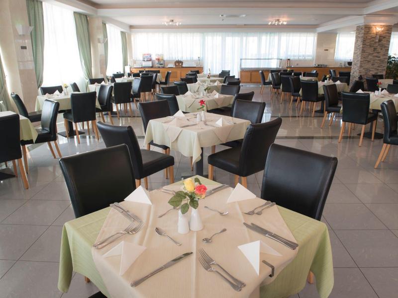 Jasna, przestronna jadalnia z nakrytymi stołami i czarnymi krzesłami.