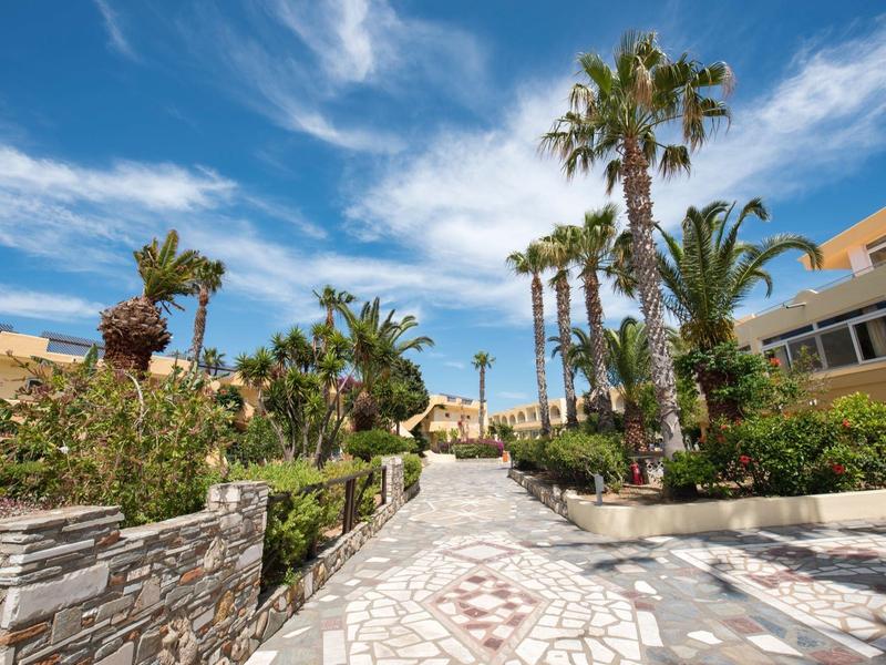 Ścieżka w otoczeniu palm i budynków pod niebieskim niebem z chmurami.