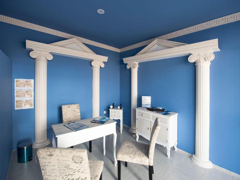 Niebieski pokój z białymi kolumnami, biurkami i krzesłami w antycznym stylu.