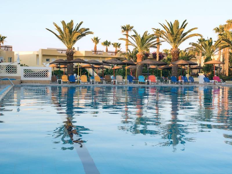 Spokojny basen hotelowy z palmami i leżakami na krawędzi o zachodzie słońca.