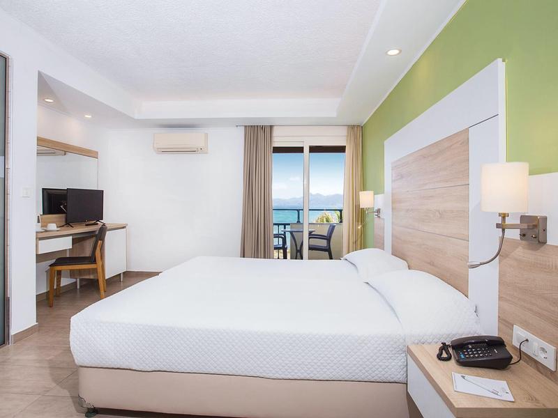 Nowoczesny pokój hotelowy z dużym łóżkiem, biurkiem, balkonem i zieloną ścianą.