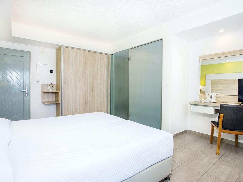 Jasny pokój hotelowy z dużym łóżkiem, drewnianą szafą, biurkiem i krzesłem.