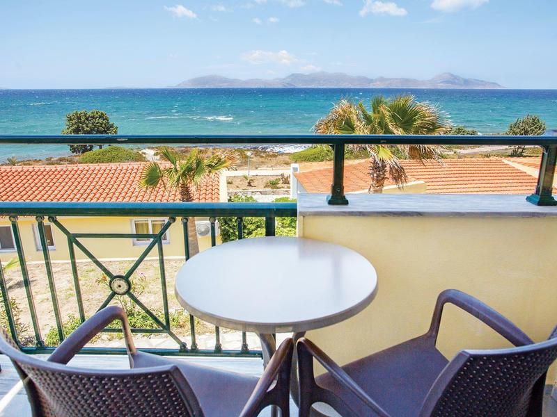 Balkon z stołem i dwoma krzesłami z widokiem na palmy i ocean pod niebieskim niebem.