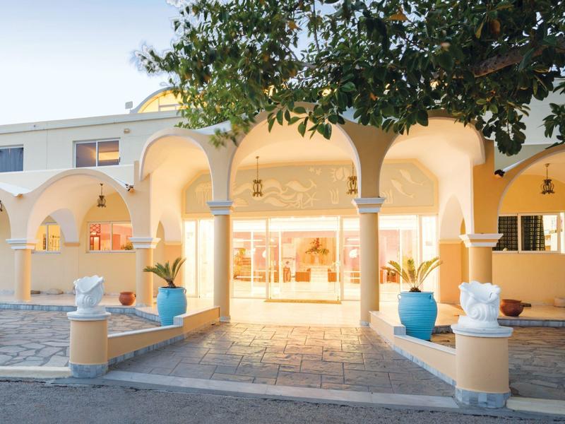 Jasne wejście do hotelu z łukami i dekoracyjnymi białymi rzeźbami w niebieskich donicach.