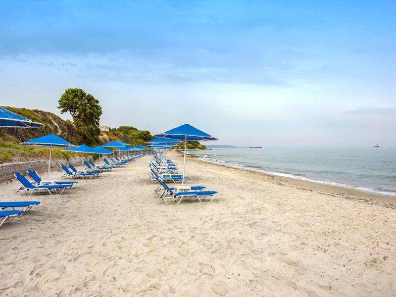 Pusta piaszczysta plaża z niebieskimi leżakami i parasolami przy spokojnym morzu.