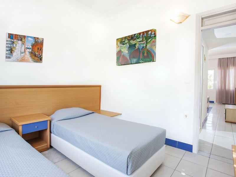 Jasny pokój z dwoma pojedynczymi łóżkami, drewnianymi zagłówkami i kolorowymi obrazami na białych ścianach.