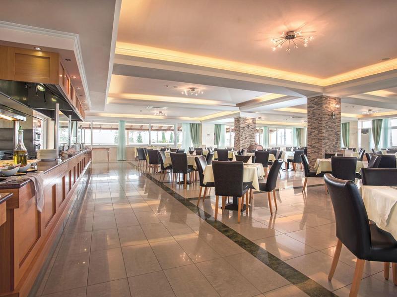 Jasna, nowoczesna restauracja z stołami, krzesłami i bufetem po lewej stronie.