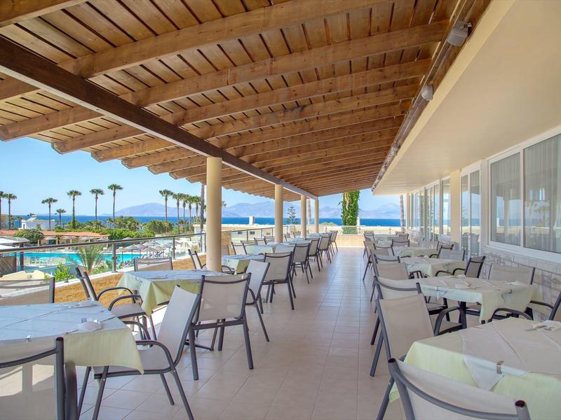 Zadaszony taras z stołami i krzesłami z widokiem na basen i morze.