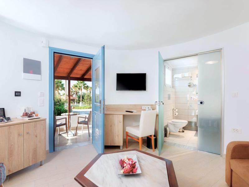 Jasny pokój hotelowy z nowoczesną łazienką, małym biurkiem i dostępem do tarasu.