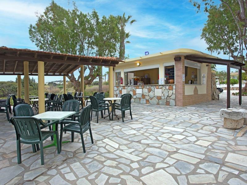 Przestrzeń na zewnątrz z stołami, krzesłami i kioskiem w słoneczny dzień.