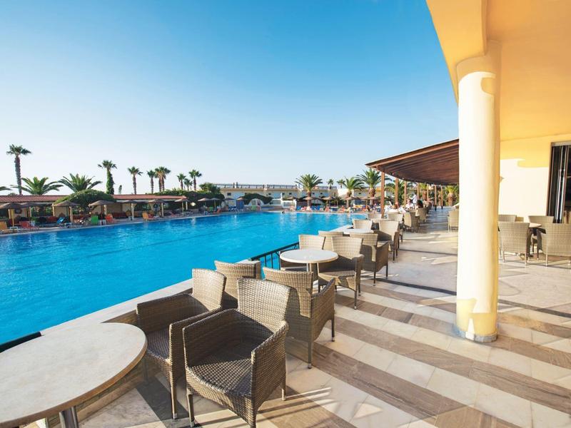 Strefa restauracyjna na świeżym powietrzu obok dużego basenu z palmami i czystym niebem.