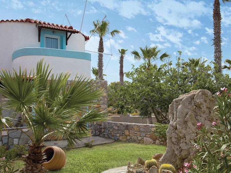 Biała willa z niebieskimi elementami przy palmach i kamiennych murach pod niebieskim niebem.