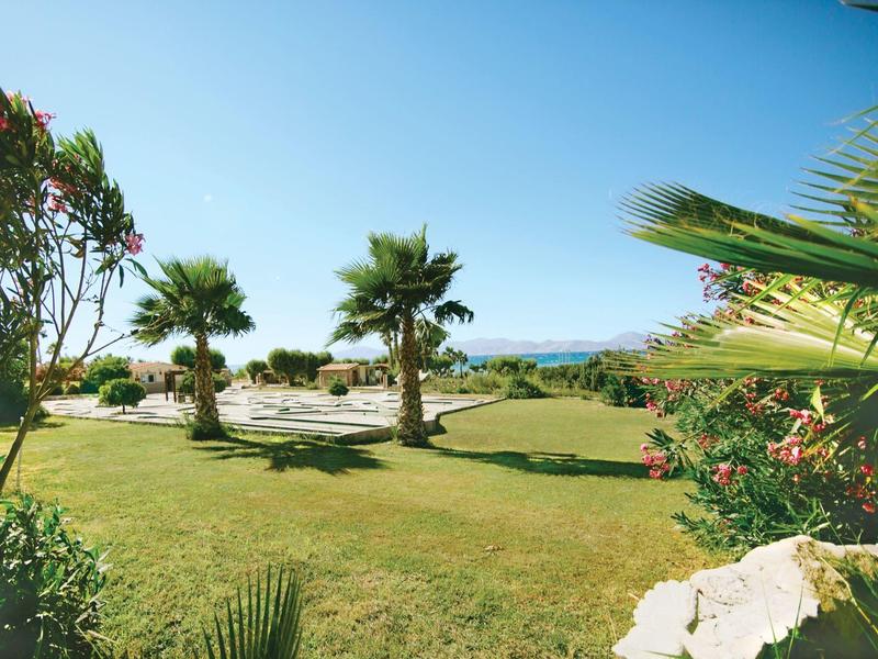 Słoneczny ogród z palmami, zielonym trawnikiem i widokiem na góry pod jasnym niebem.