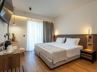 Modernes Hotelzimmer mit Doppelbett, Holzfußboden und Balkon mit Vorhängen.